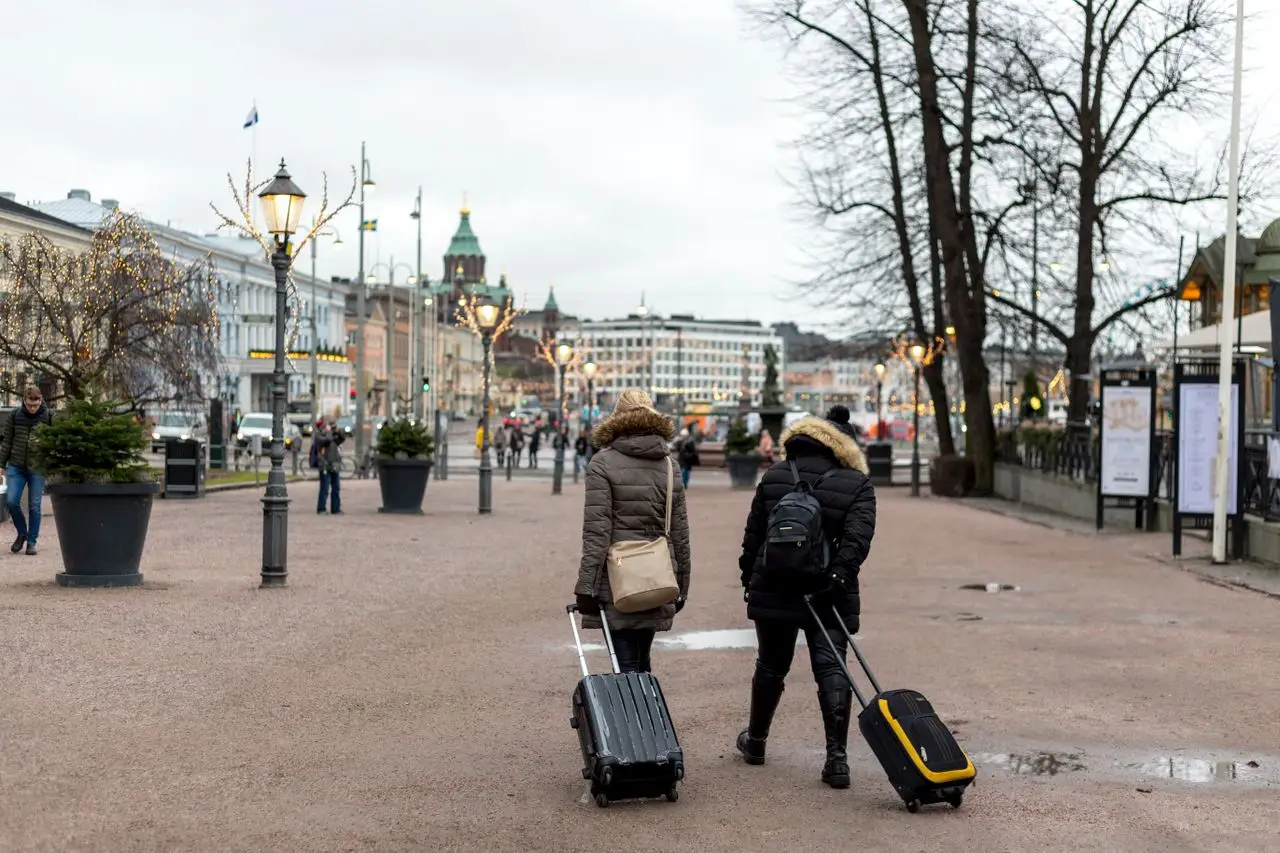 Tourists with luggage stroll through Helsinki on a cloudy day.